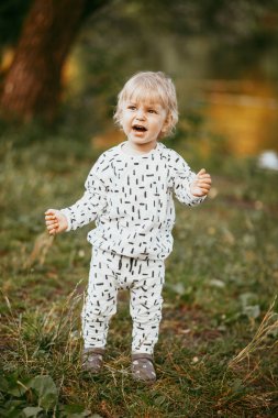 Doğanın arka planına karşı güzel beyaz bir takım elbiseyle yürüyen tatlı bir çocuk. Bir yaşında bir çocuk öğreniyor ve dışarıda oynuyor..
