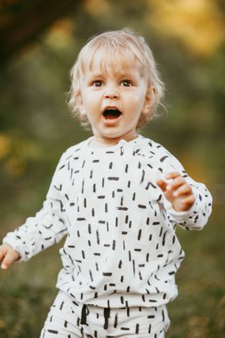 Doğanın arka planına karşı güzel beyaz bir takım elbiseyle yürüyen tatlı bir çocuk. Bir yaşında bir çocuk öğreniyor ve dışarıda oynuyor..