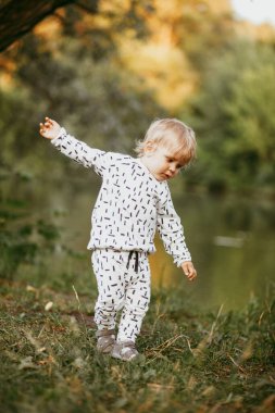 Doğanın arka planına karşı güzel beyaz bir takım elbiseyle yürüyen tatlı bir çocuk. Bir yaşında bir çocuk öğreniyor ve dışarıda oynuyor..