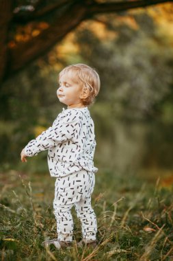Doğanın arka planına karşı güzel beyaz bir takım elbiseyle yürüyen tatlı bir çocuk. Bir yaşında bir çocuk öğreniyor ve dışarıda oynuyor..