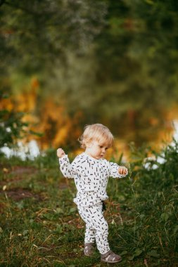 Doğanın arka planına karşı güzel beyaz bir takım elbiseyle yürüyen tatlı bir çocuk. Bir yaşında bir çocuk öğreniyor ve dışarıda oynuyor..