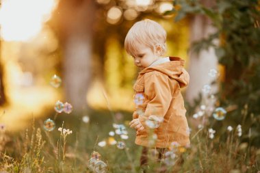 Bir sonbahar günü, gün batımında bej ceketle yürüyen tatlı bir erkek bebek.
