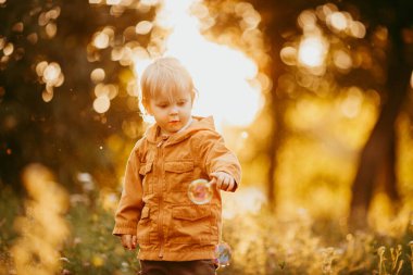 Bir sonbahar günü, gün batımında bej ceketle yürüyen tatlı bir erkek bebek.