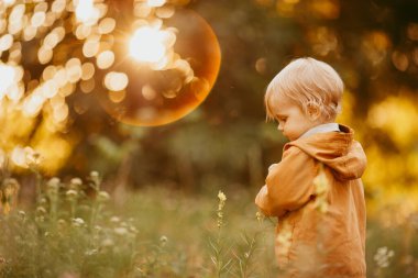 Bir sonbahar günü, gün batımında bej ceketle yürüyen tatlı bir erkek bebek.