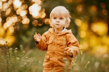 Bir sonbahar günü, gün batımında bej ceketle yürüyen tatlı bir erkek bebek.