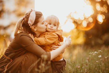 Genç bir anne oğlunun yürümesine yardım eder. Bir anne oğluna öğretir, eğitir ve onunla ilgilenir. Yaz günü.