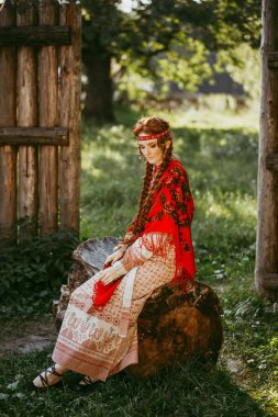 Uzun sarı saçlı, kahverengi gözlü, beyaz ve kırmızı işlemeli takım elbiseli ve omuzlarında kırmızı elbiseli güzel bir Slav kız. Ukrayna bölgesinin geleneksel kıyafetleri. Yaz günü.