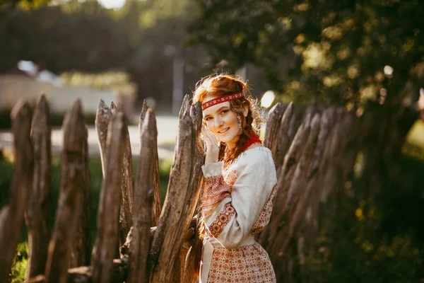 白と赤の刺繍のスーツで長いブロンドの髪と茶色の目を持つ美しいスラブの女の子は 木製のフェンスで立っています ウクライナ地域の伝統的な服 夏の日 — ストック写真