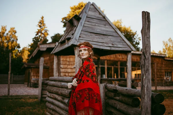白と赤の刺繍のスーツで長いブロンドの髪と茶色の目を持つ美しいスラブの少女は 木造の家の隣に座っています ウクライナの地域の伝統的な服 夏の日 — ストック写真