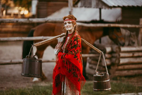 白と赤の刺繍のスーツで長いブロンドの髪と茶色の目を持つ美しいスラブの少女は 木造の家の隣に座っています ウクライナの地域の伝統的な服 夏の日 — ストック写真