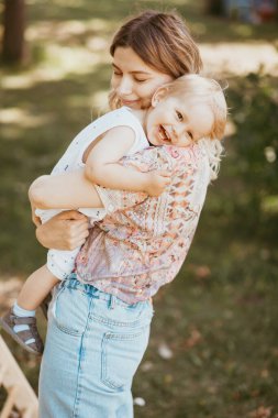 Genç bir anne, güzel bir yaz parkında, gülümseyen bir yüzle oğluna sarılıyor. Aile bir ağacın altında dinleniyor, birlikte eğleniyor. Anneler günü aşkı, anneler günü konsepti..