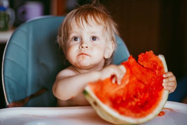 Mutlu bebek evdeki sandalyesinde karpuz yiyor.