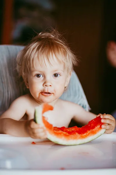 Счастливый малыш ест арбуз в своем стульчике — стоковое фото