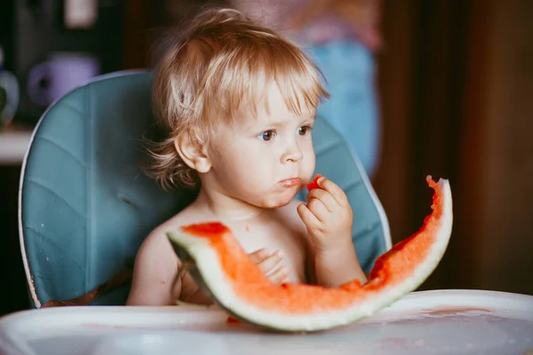 Menino feliz comendo melancia em sua cadeira alta — Fotografia de Stock