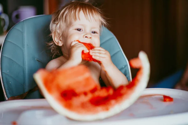 Menino feliz comendo melancia em sua cadeira alta — Fotografia de Stock