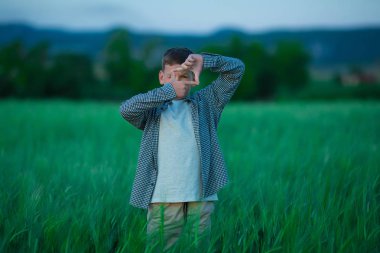Sevimli küçük yakışıklı çocuk fotoğraf makinesi ile poz rahat kıyafetlerle ve yeşil alan taze çavdarlı ayakta parmak.