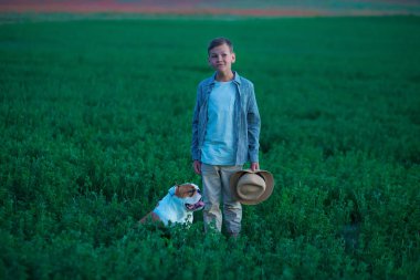Onun İngilizce boğa köpek yeşil çavdar çayır üzerinde küçük çocuk oturma dururken. Şık giysiler ve rustik retro şapka giyen en iyi arkadaşıyla poz Handsom çocuk.