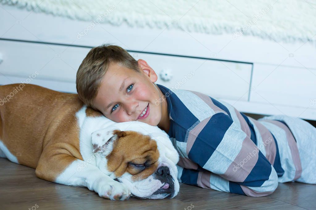 Handsome Young Boy kid wearing cozy pajamas Playing with His english funny bull Dog on the floor enjoy life time weekend hanging each other with love and tender.