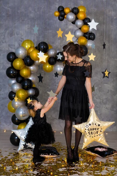 Woman power party with beautiful model mother and cute baby daughter dressed in airy black fancy dresses celebrating love with golden stars and air baloons. Pillow stars SUPER STAR designed by photographer