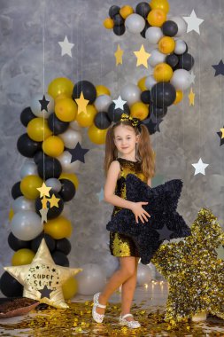 Movie super star girl model posing in studio shoot with golden star and colorful baloons wearing stylish gold airy dress with shining bow tie.Super star pillow deisigned by photographer clipart