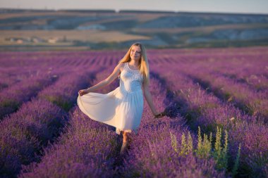 Güzel sarışın Bayan model lavanta alan üzerinde gülümseyen keyfini yaz günü buket çiçek ile havadar beyaz elbise