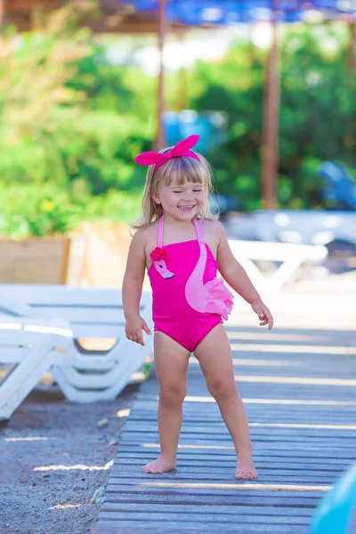 Baby girl on beach with pink flamingo dressed in stylish swimming wear posing on wooden floor. Scene on vacation on sea side of a cute lady smiling and enjoy life time childhood infancy