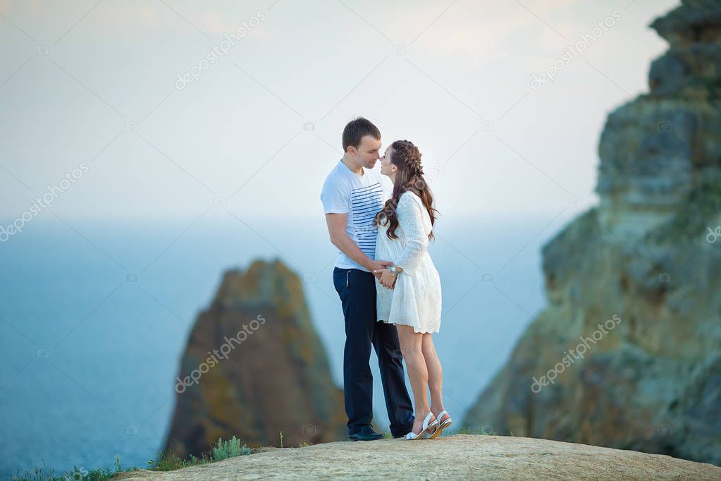 Beautiful young couple expecting baby posing on mountain view with blue sea as background.