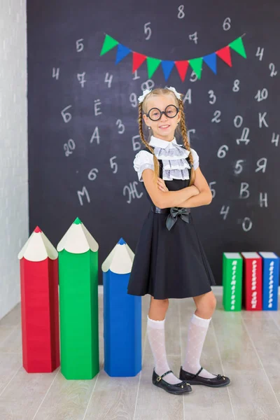 The schoolgirl in school uniform with books and textbooks is on a light gray background. Back to school. The new school year. Child education concept
