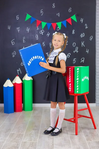The schoolgirl in school uniform with books and textbooks is on a light gray background. Back to school. The new school year. Child education concept