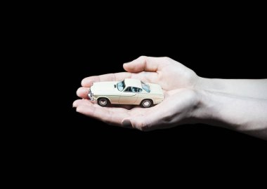 Klasik retro oyuncak araba modeli siyah arka plan önünde tutan eller