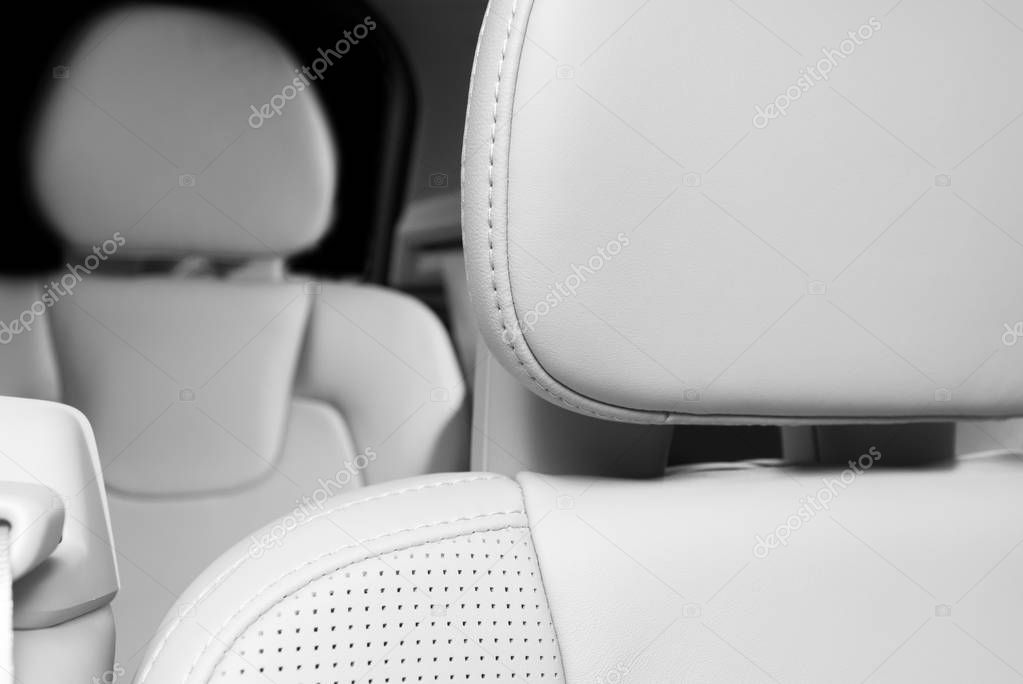 Part of white perforated leather car seat with the unfocused car interior on the background