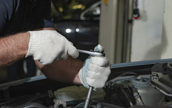 Close up hands in white textile gloves of mechanic doing car service and maintenance in a car repair garage