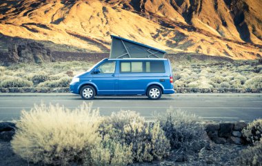 Küçük seyahat aracı kamp minibüsü ya da çatısı katlanır yataklı büyük araba büyük dağ düzeninin altına park edilmiştir. Turizm tatili ve seyahat. Kamp aracı ve dağ manzarası