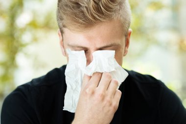 Grip olmuş güzel bir adamın portresi. Adam parkta burnunu siliyor.