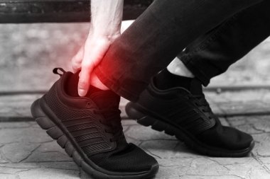 Bileğim burkuldu. Genç adam parkta burkulmuş bacağına dokunuyor. Kırmızı aksanlı siyah beyaz