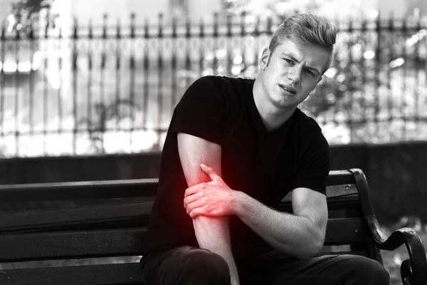 Elbow pain. Man in the park holding his aching elbow . Black and white with a red accent