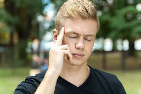 Portrait of a pretty man with stress and headache having migraine pain in the park