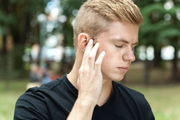 Man has a sore ear.  Man suffering from otitis in park