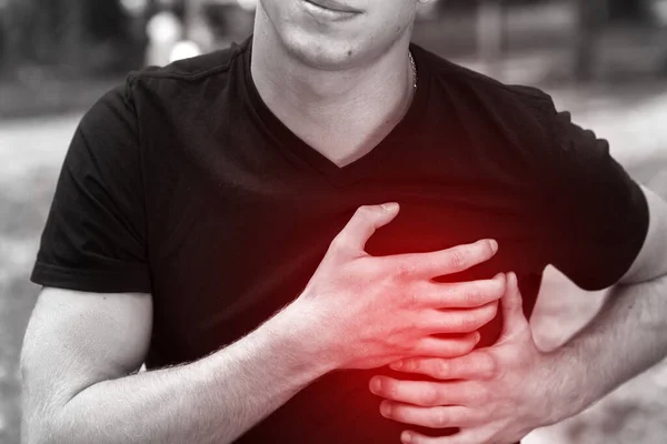 Outdoor portrait of a  man  with heart attack or broken heart  standing in the park. Black and white with a red accent