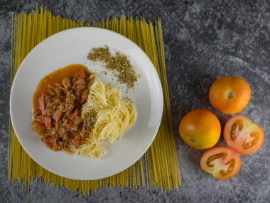 Olgun pişmiş makarna spagetti domates sosu kekik beyaz tabak içinde. pişmemiş makarna ve domates yanında.