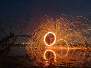 light lines of steel wool with long exposure, speed motion abstract background in the dark night with dry branch tree and reflection in water,look like dick penis