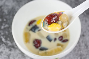 Soya süt ilave maddeler ile siyah çim jöle, ginkgo, longan, kırmızı fasulye, tohum, Tayland yerel ünlü sokak beyaz kaşık ve gıda kase beton zemin üzerine Özet