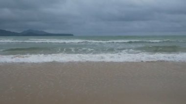 Yumuşak dalga deniz suyu, bulutlu yağmurlu gökyüzü güzel kum plaj.