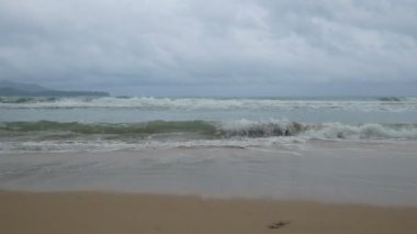 Yumuşak dalga deniz suyu, bulutlu yağmurlu gökyüzü güzel kum plaj.