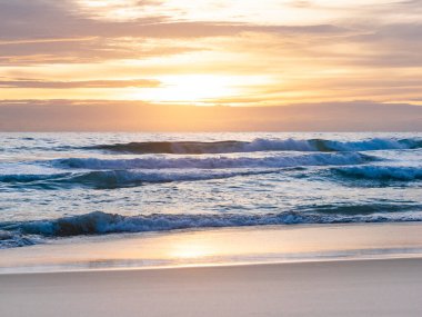 Kumsala vuran deniz dalgası, gün batımında bulutlu gökyüzü.