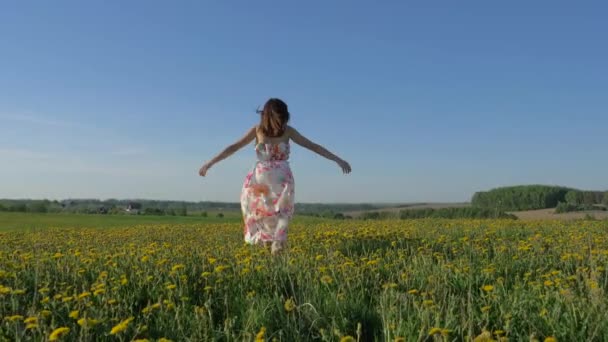 Sorrindo feliz mulher andando em um campo amarelo florescendo em um vestido girando — Vídeo de Stock