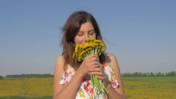 Porträtt av kvinna i fältet med bukett gul maskros blommor sniffar honom — Stockvideo