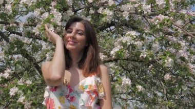 Çiçek açan bir elma meyve bahçesinde duran genç bir beyaz kadın portresi