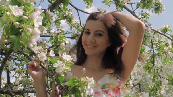 Porträt einer jungen hübschen kaukasischen Frau, die in einem blühenden Apfelgarten steht — Stockvideo