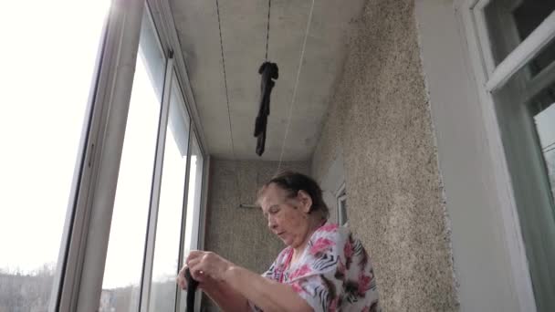 Gammal kvinna hänger tvätt på balkong eller Veranda för torkning — Stockvideo